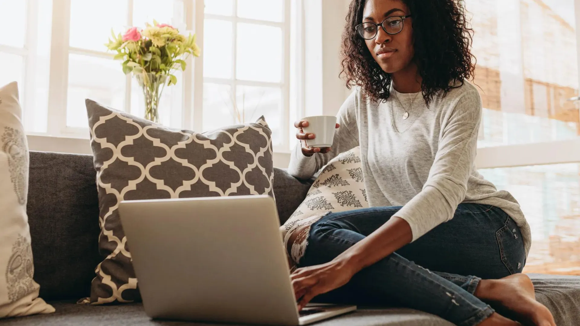 Woman sitting on couch holding coffee cup looking at her computer