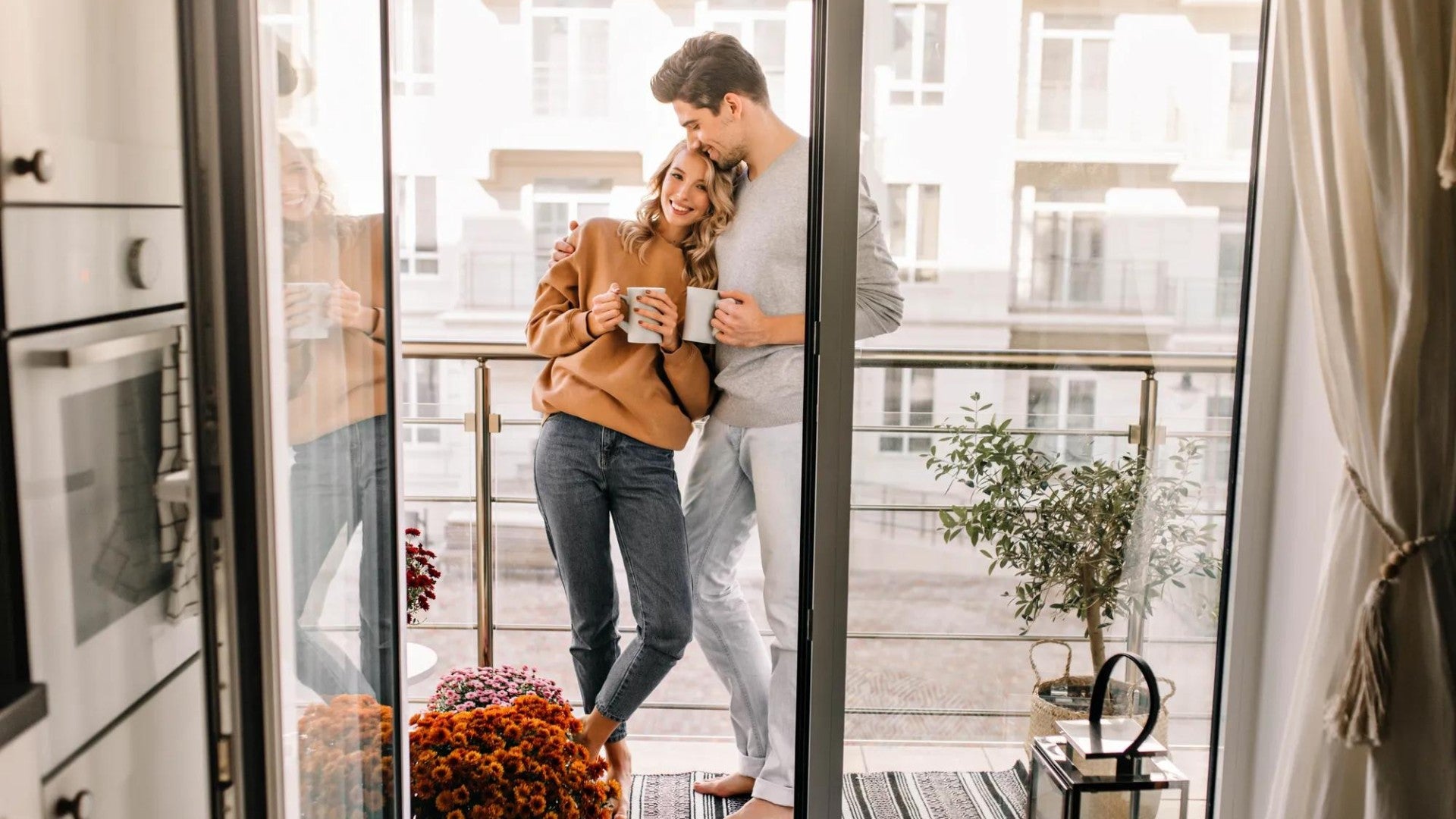 Man and woman standing in the sunlit kitchen happily with coffee mugs