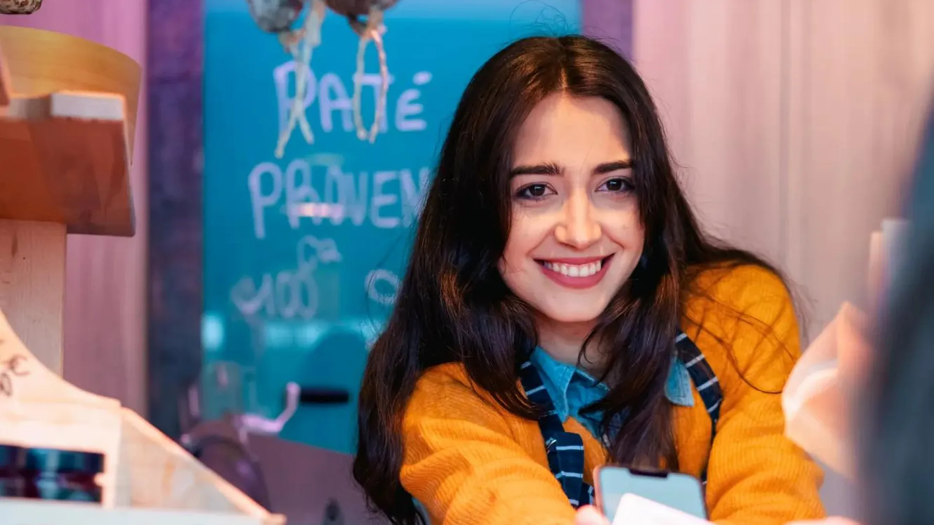 A young woman behind the counter at a butcher shop receives a digital payment from a customer. 