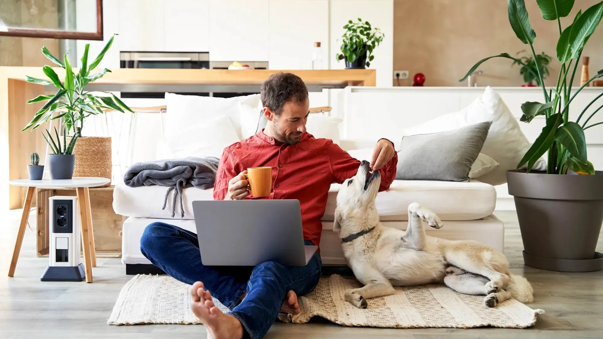 Man, sitting on floor looking at computer, with his dog