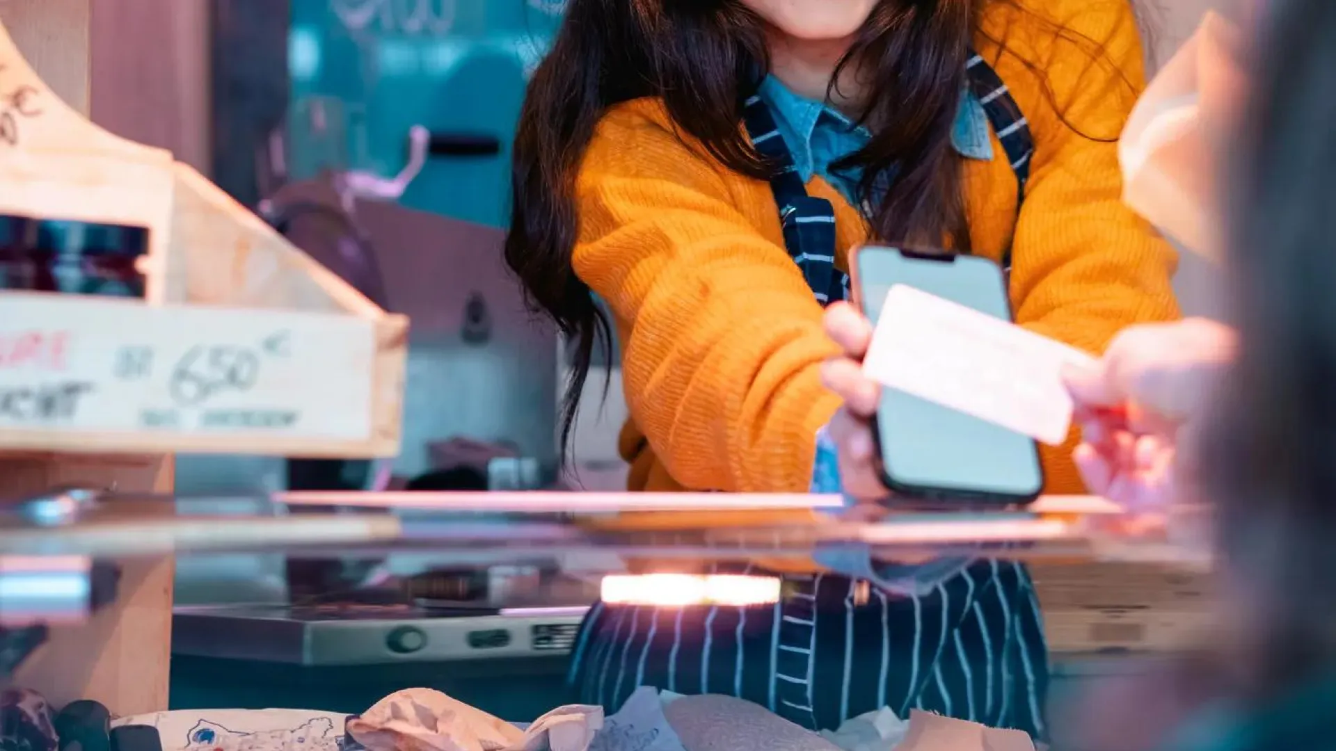 A young woman behind the counter at a butcher shop receives a digital payment from a customer. 