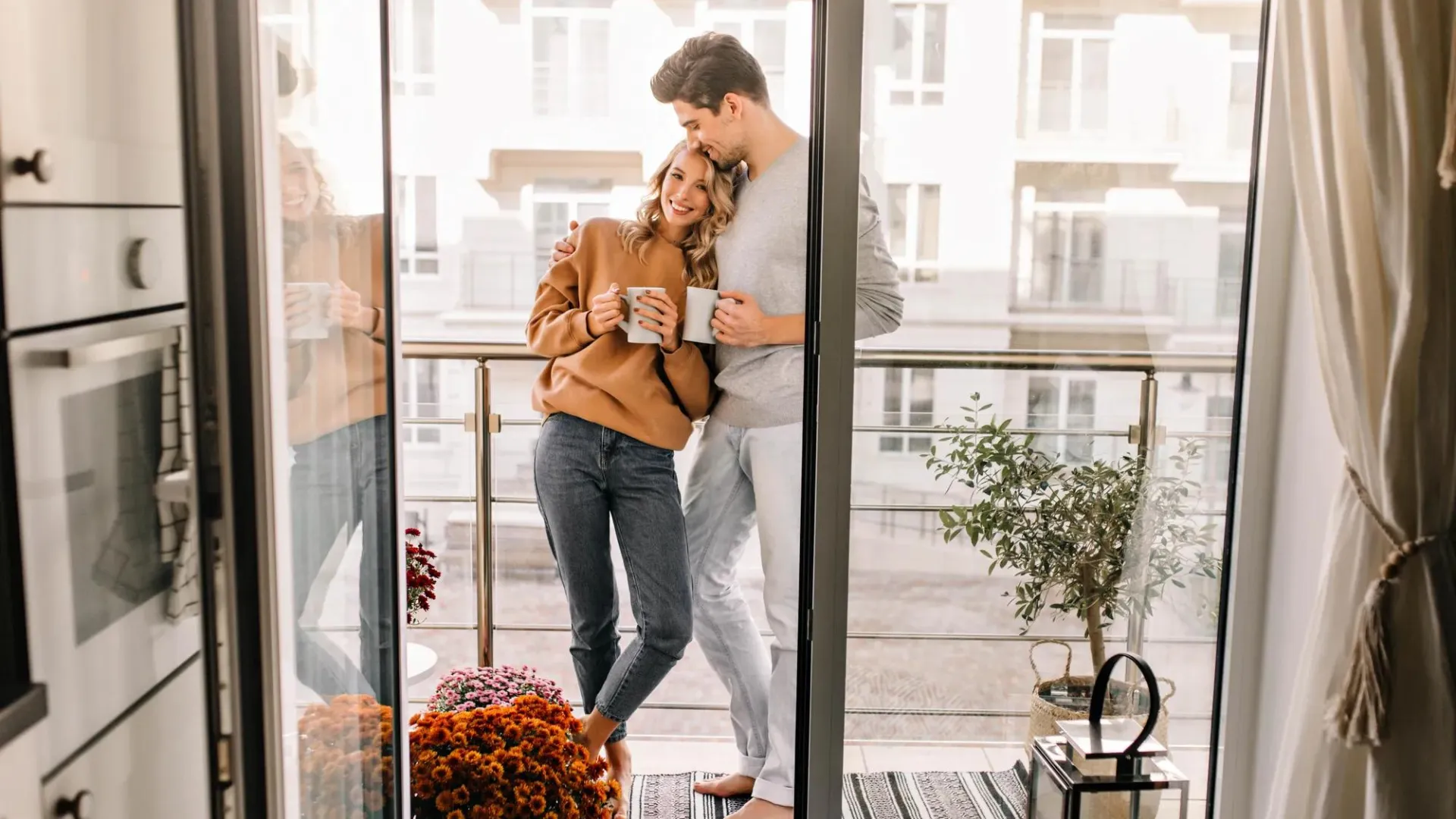 Man and woman standing in the sunlit kitchen happily with coffee mugs