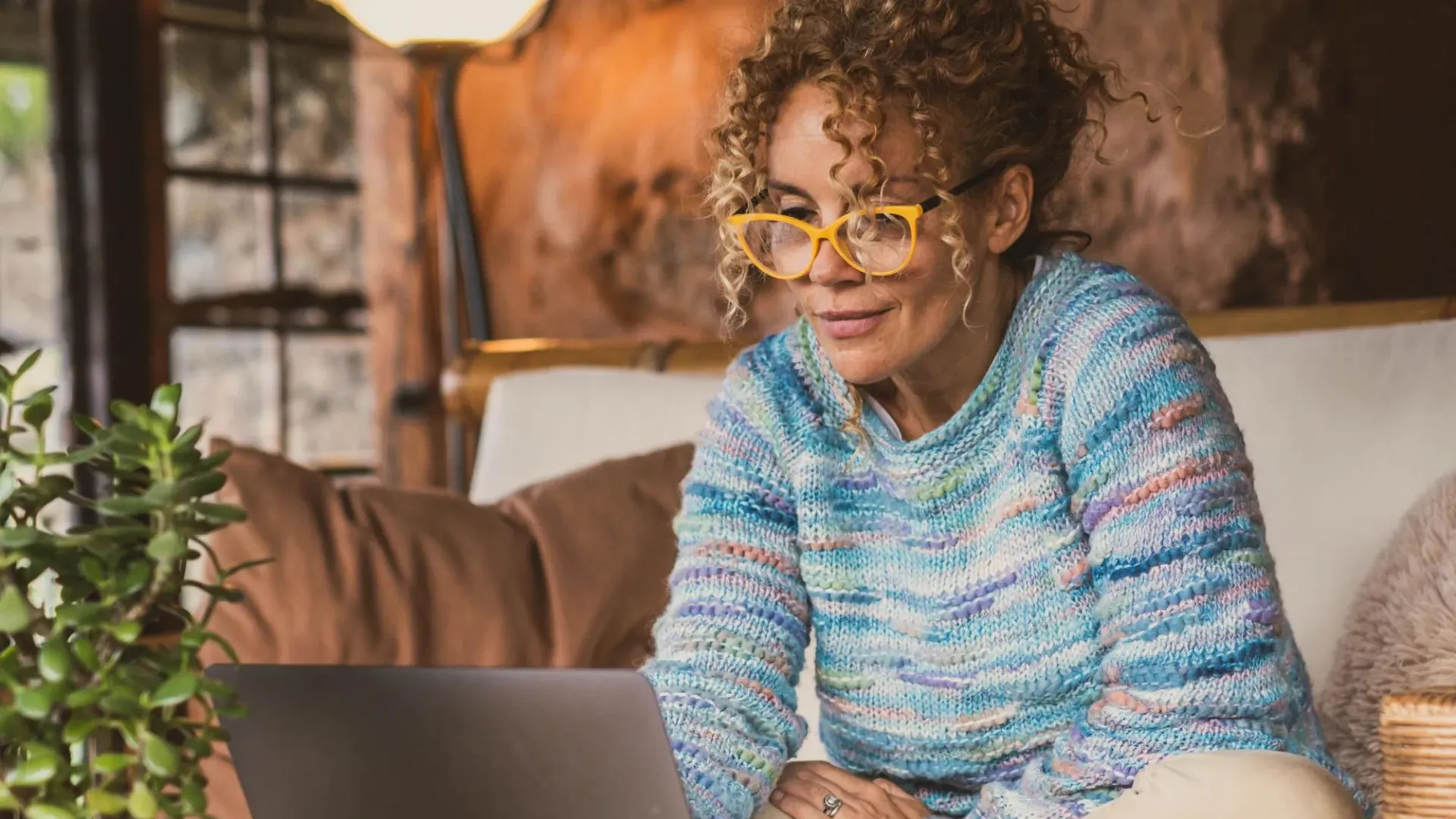 Happy modern woman at home sitting on the sofa using a laptop and wearing eyewear.