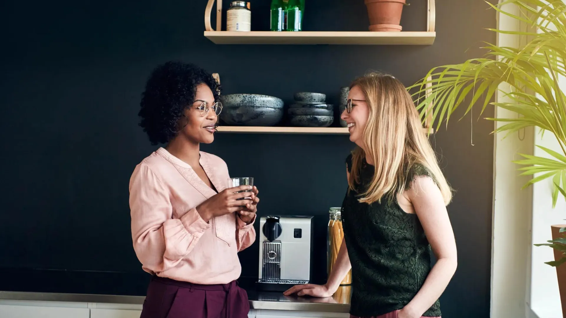 Two employees chatting near office espresso machine.