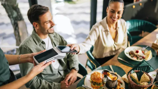 Woman paying for meal by phone app while out to eat with friends.