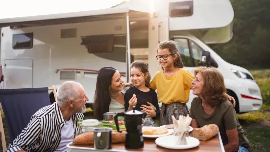 Grandparents, mom, and two daughters eating at table outside with RV in background