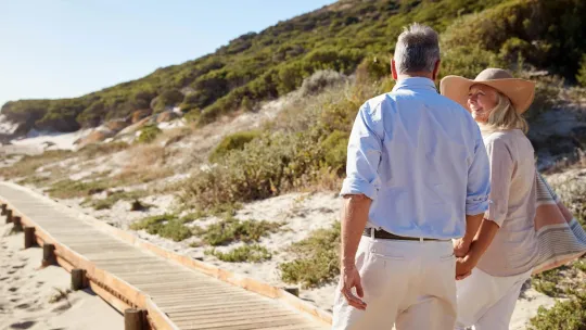 Older couple walking on sidewalk on beach.