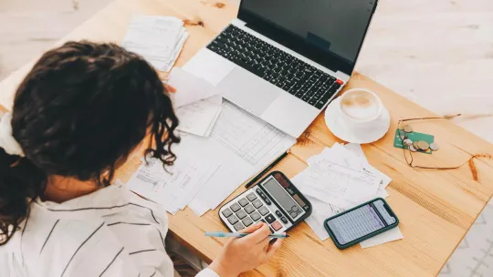 Woman working on taxes and retirement planning using calculator and notebook.