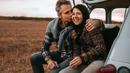 Middle aged couple sitting on the trunk of a car.