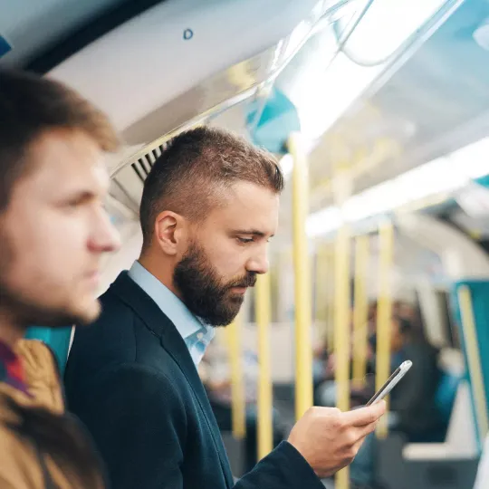 Man in a subway train looking at his mobile phone, reviewing his account balance in the mobile app.