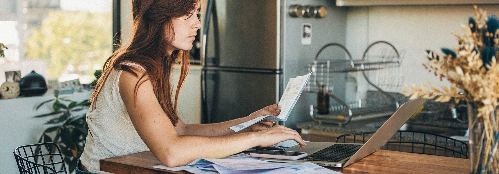 Photo of woman sitting in her kitchen, filing her taxes on her laptop.