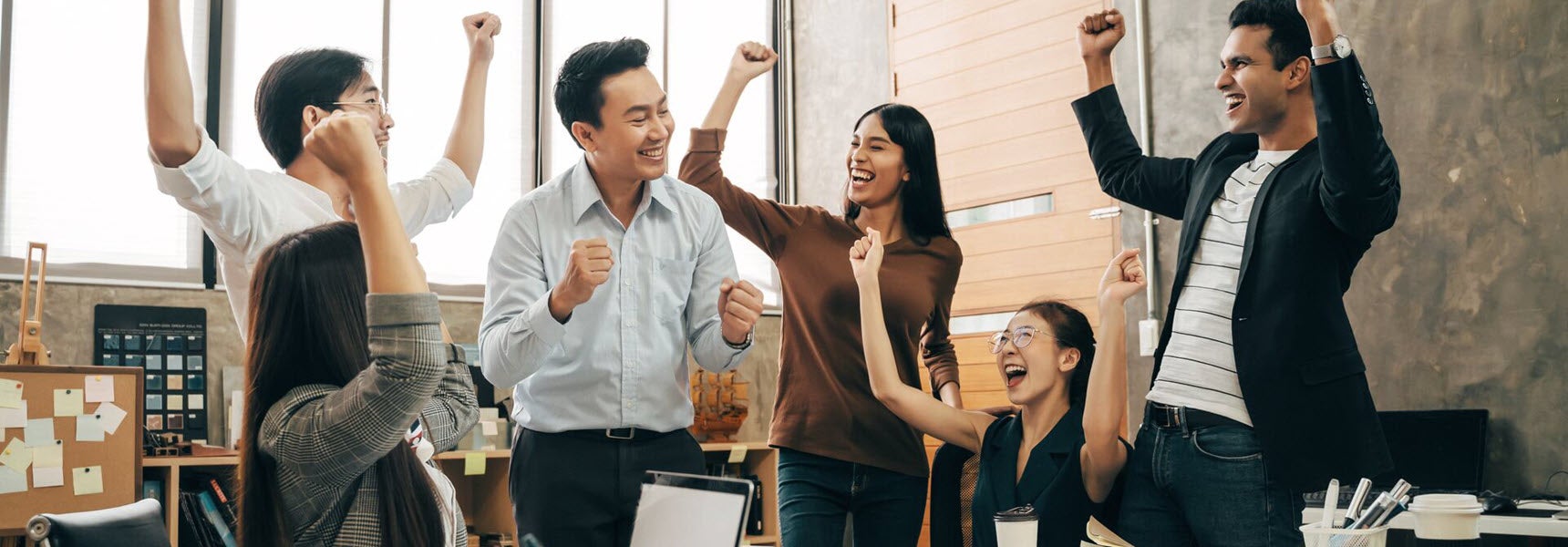 Smiling employees in an office raise their arms in celebration.