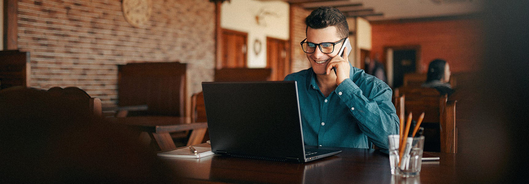 Photo of a man on a computer talking on his cell phone.