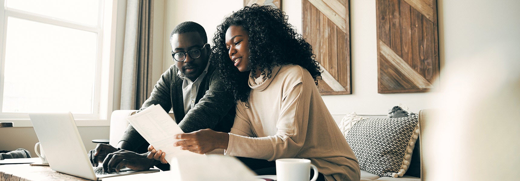 Photo of a couple sitting on the couch in their living room reviewing documents related to their investments.