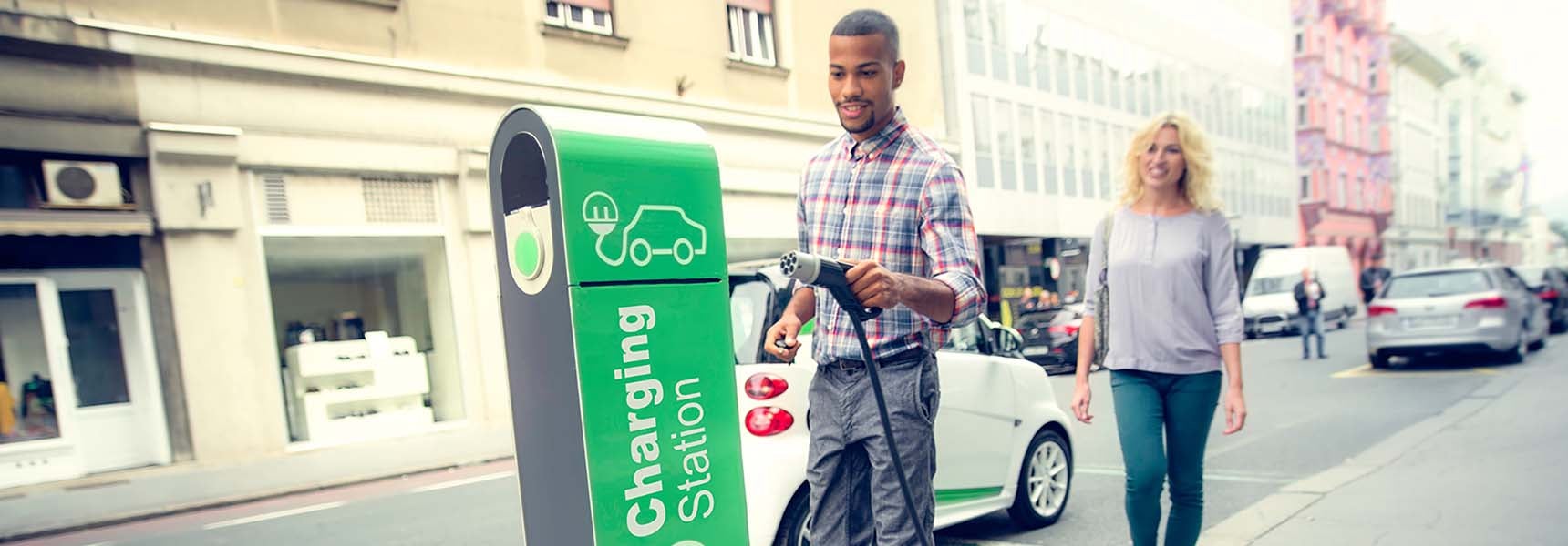 Photo of a man and a woman plugging in their electric vehicle.