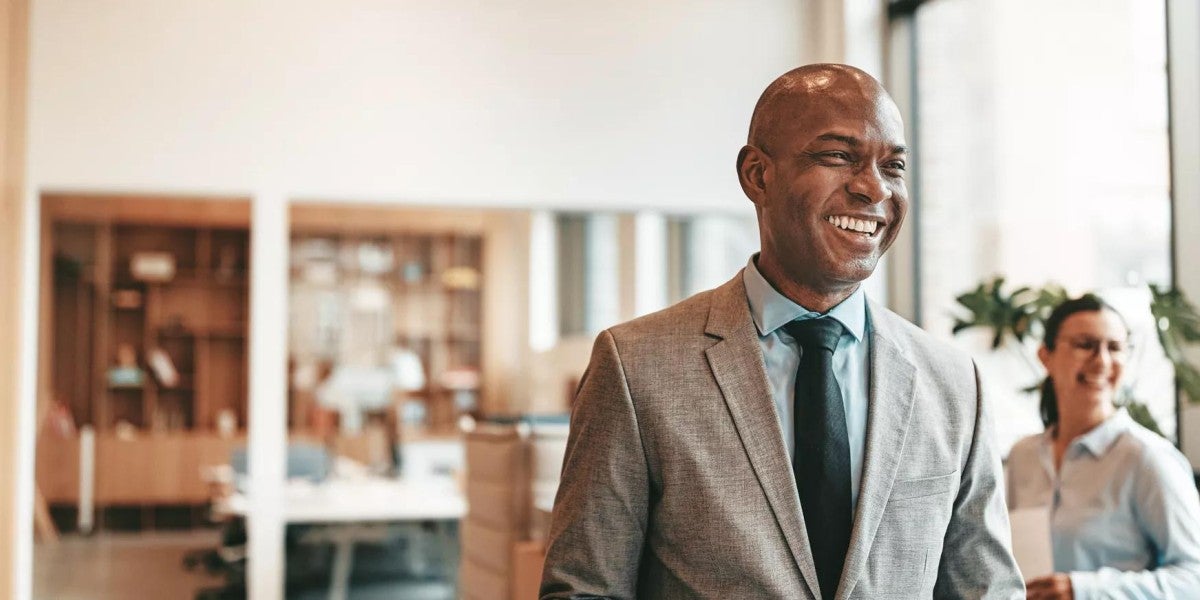 Confident businessman in a suit and tie smiles while walking through a modern office.