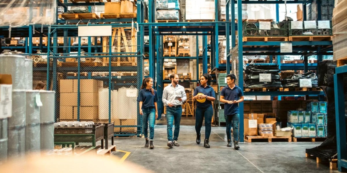 A group of four warehouse employees walking through an aisle of storage racks and talking