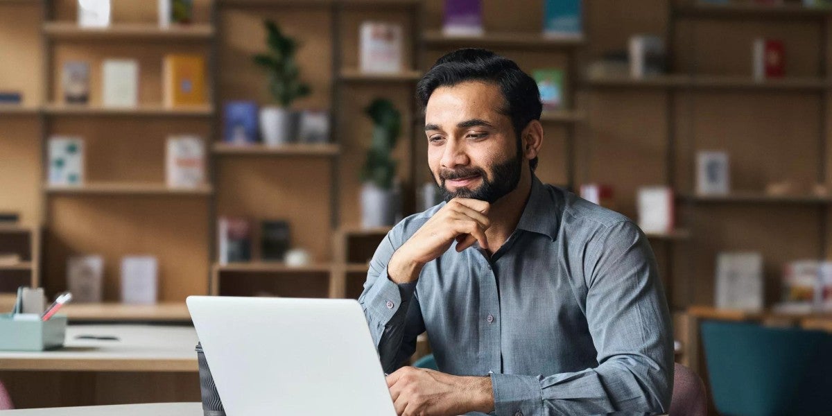 Bearded Indian business man watching online webinar on laptop computer.