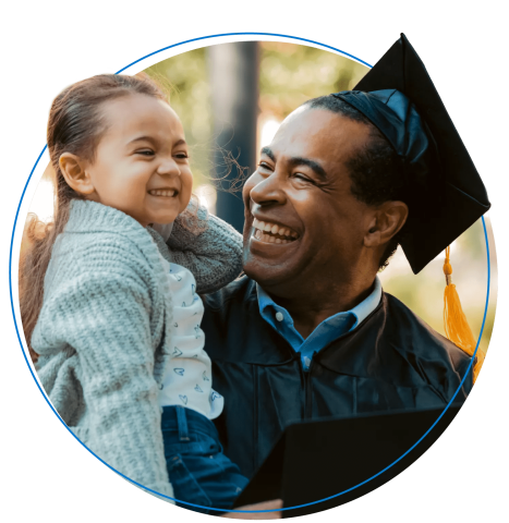 Graduating dad wearing a cap and gown smiles while holding daughter