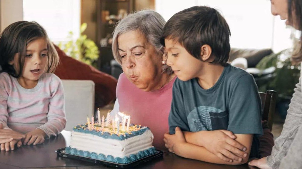 An older adult is blowing out the candles on her birthday cake while her family watches.