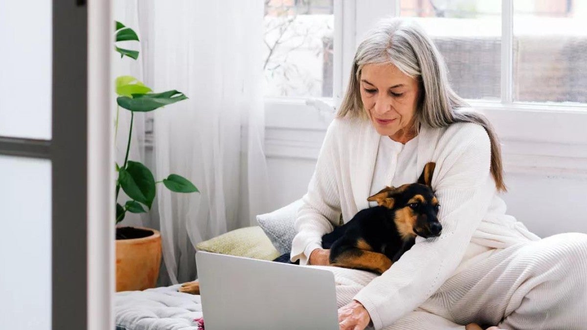 Elderly woman with dog working on laptop