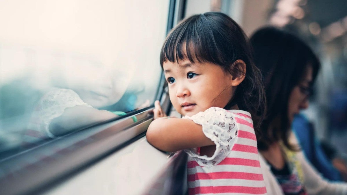 A young girl looks out the window of a passenger train.