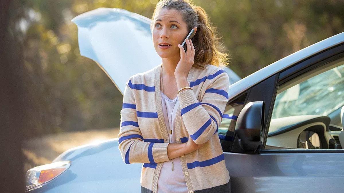 A woman looking at her broken down vehicle happy she has an emergency fund.