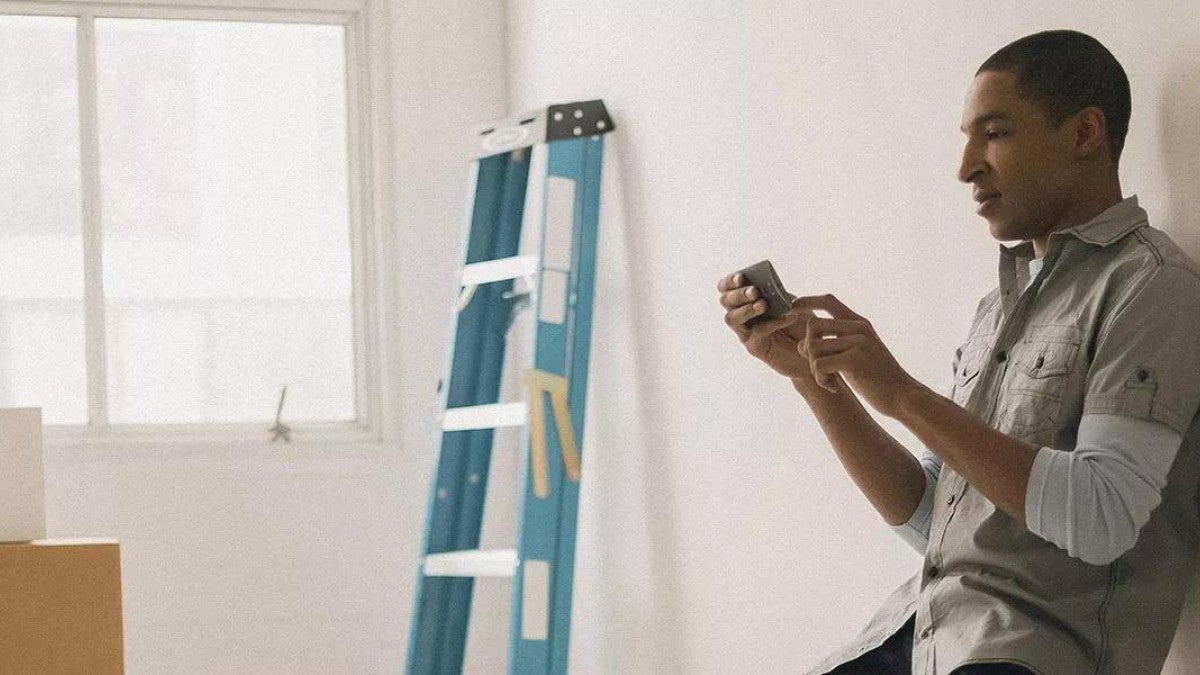 Photo of man leaning against the wall looking at his phone and thinking about his investment risk.