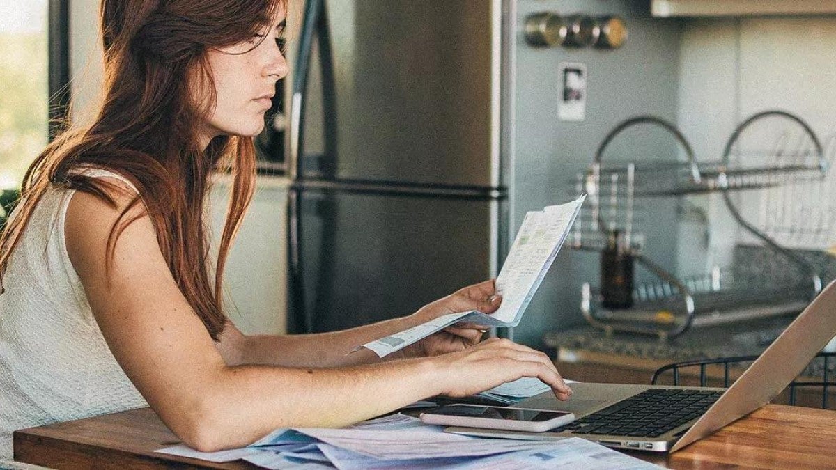 Photo of woman sitting in her kitchen, filing her taxes on her laptop.