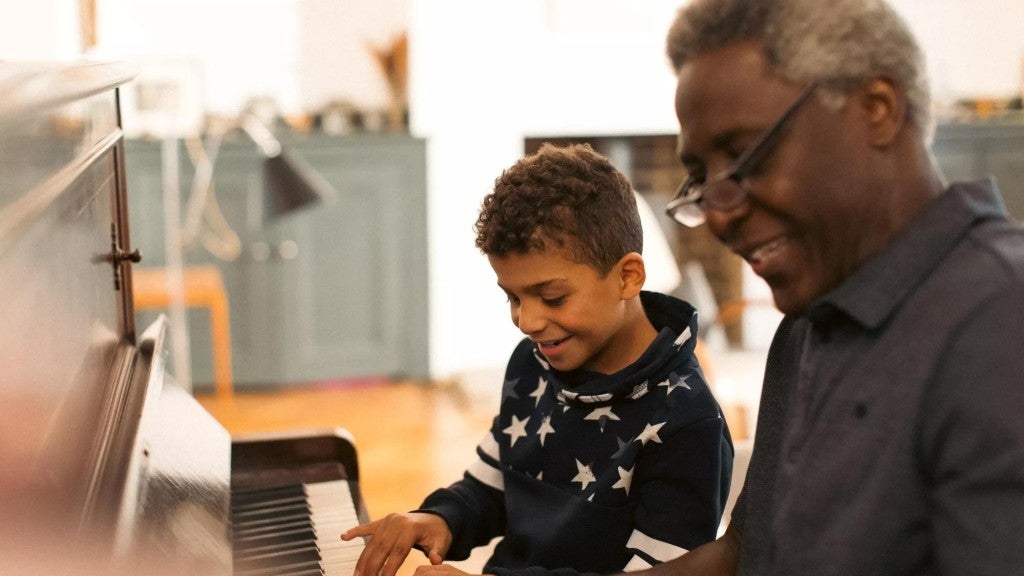 Grandfather smiles while playing the piano with his son