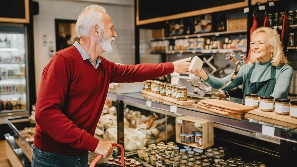 Retiree at a grocery market, collecting a block of cheese at a deli counter.