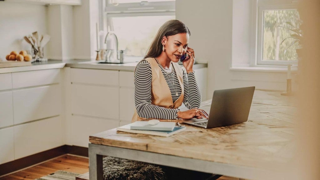 Woman at home working on computer and talking on cellphone.