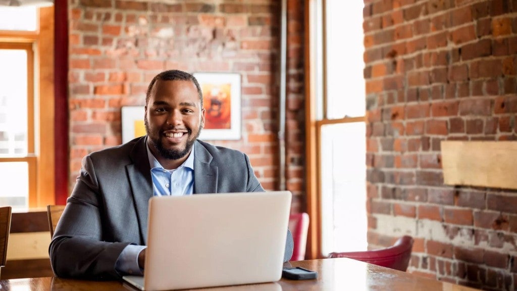 Black adult male sitting at table with his laptop