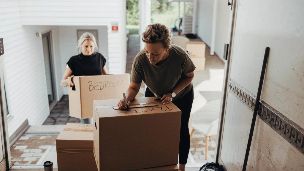 Woman holding box while female writing on cardboard box in moving van