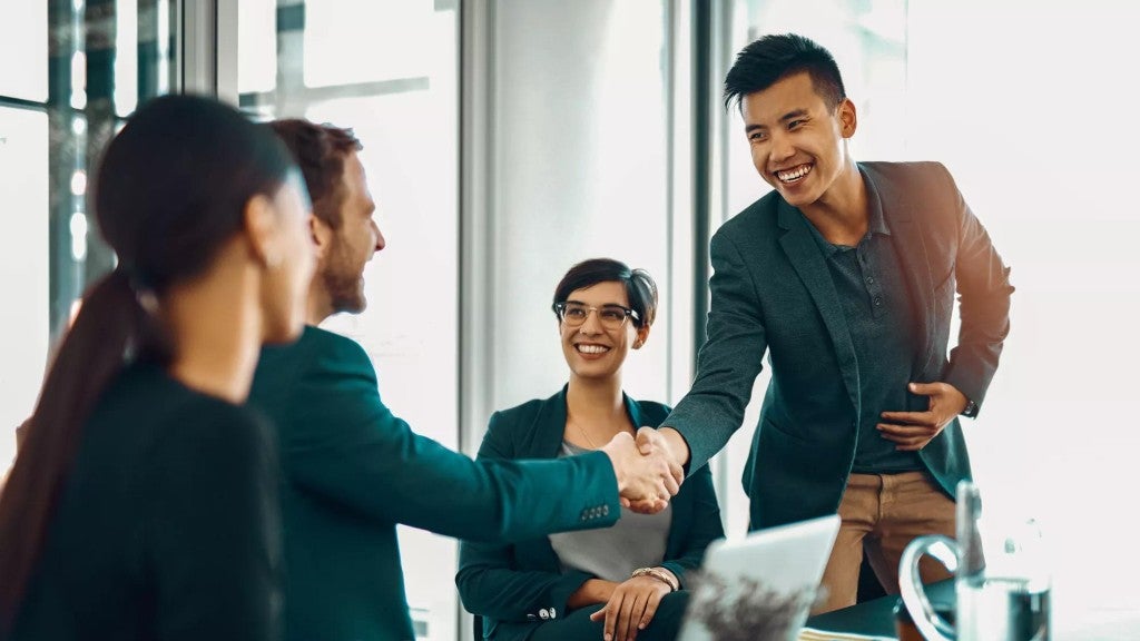 A group of workers shaking hands as they sit at a worktable.