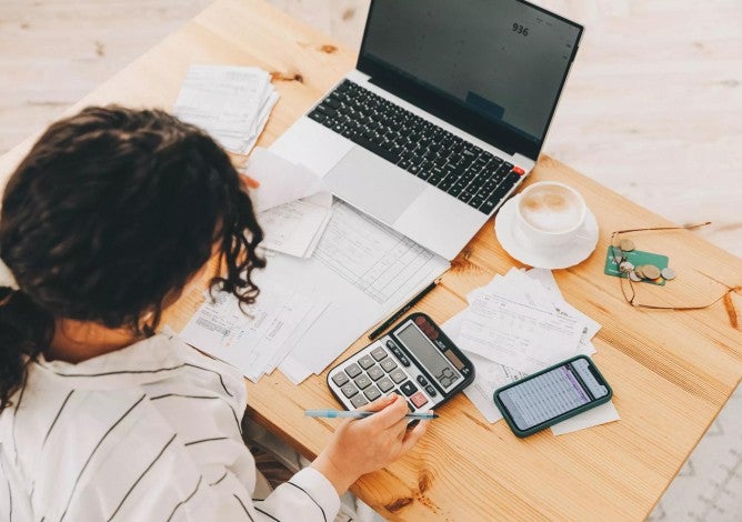 Woman working on taxes and retirement planning using calculator and notebook.