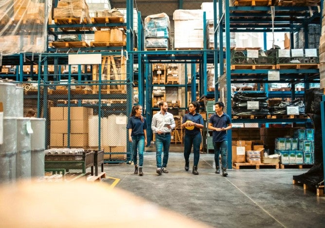A group of four warehouse employees walking through an aisle of storage racks and talking