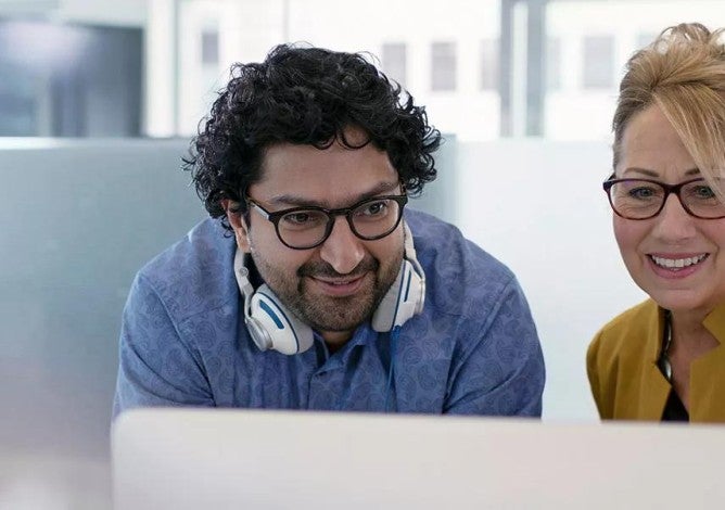 Two smiling coworkers looking at the same screen.