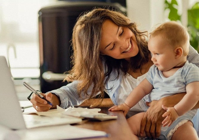 Photo of woman smiling at baby while she works on a laptop.