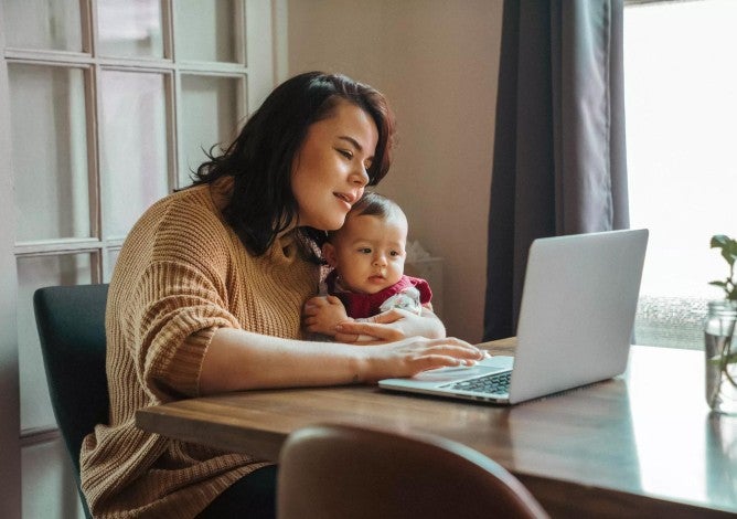 Mujer sosteniendo a un bebé en su regazo y mirando su puntaje crediticio en una computadora.