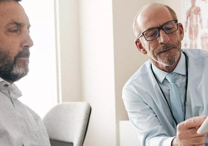 A patient in a doctor's office looks at a tablet a doctor is holding while the doctor explains what he is seeing.