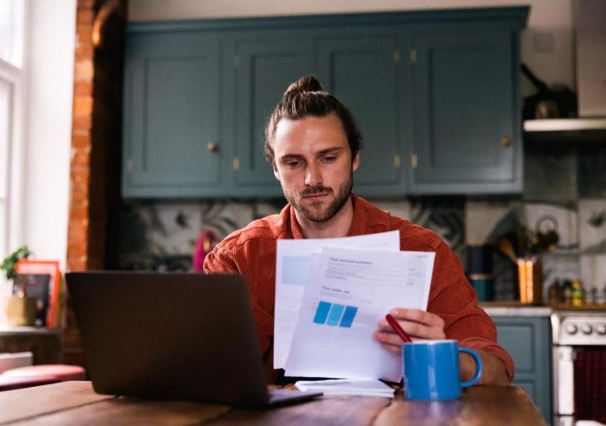 Young adult male at home looking at bills and personal finances using a laptop.