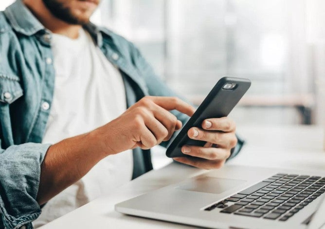 Un hombre revisando su teléfono y computadora