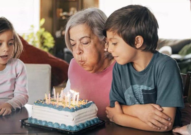 An older adult blowing out the candles on her birthday cake while her family watches.