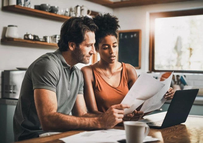 Man and woman seated at a kitchen table looking at retirement contributions on a laptop computer