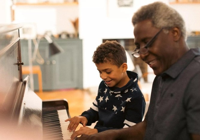 Grandfather smiles while playing the piano with his son
