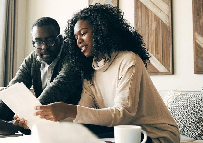 A couple sitting on the couch in their living room reviewing documents related to their investments.