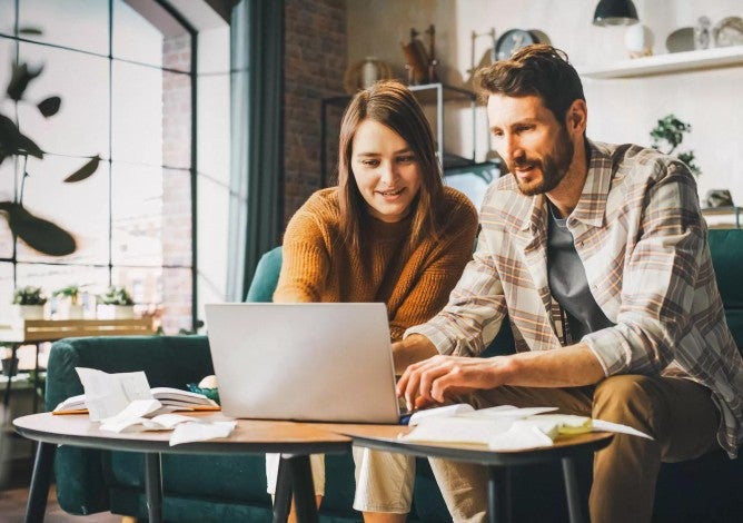 Hombre y mujer sentados en un sofá mirando las condiciones de inversión en una computadora portátil.