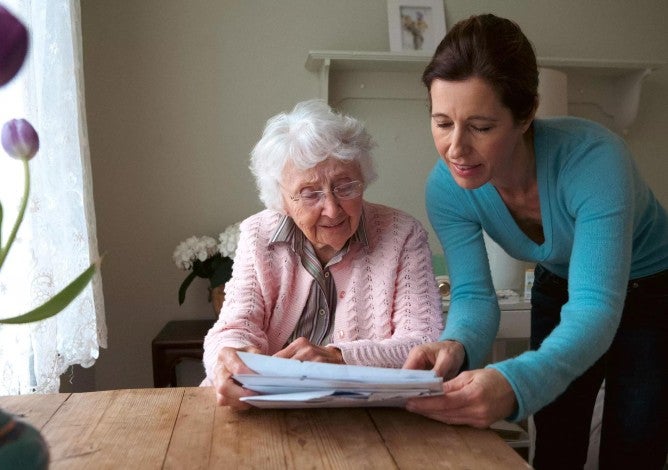 Woman reading to her mother at the table.