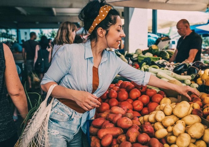 A young woman buys vegetables and fruits at the market . 